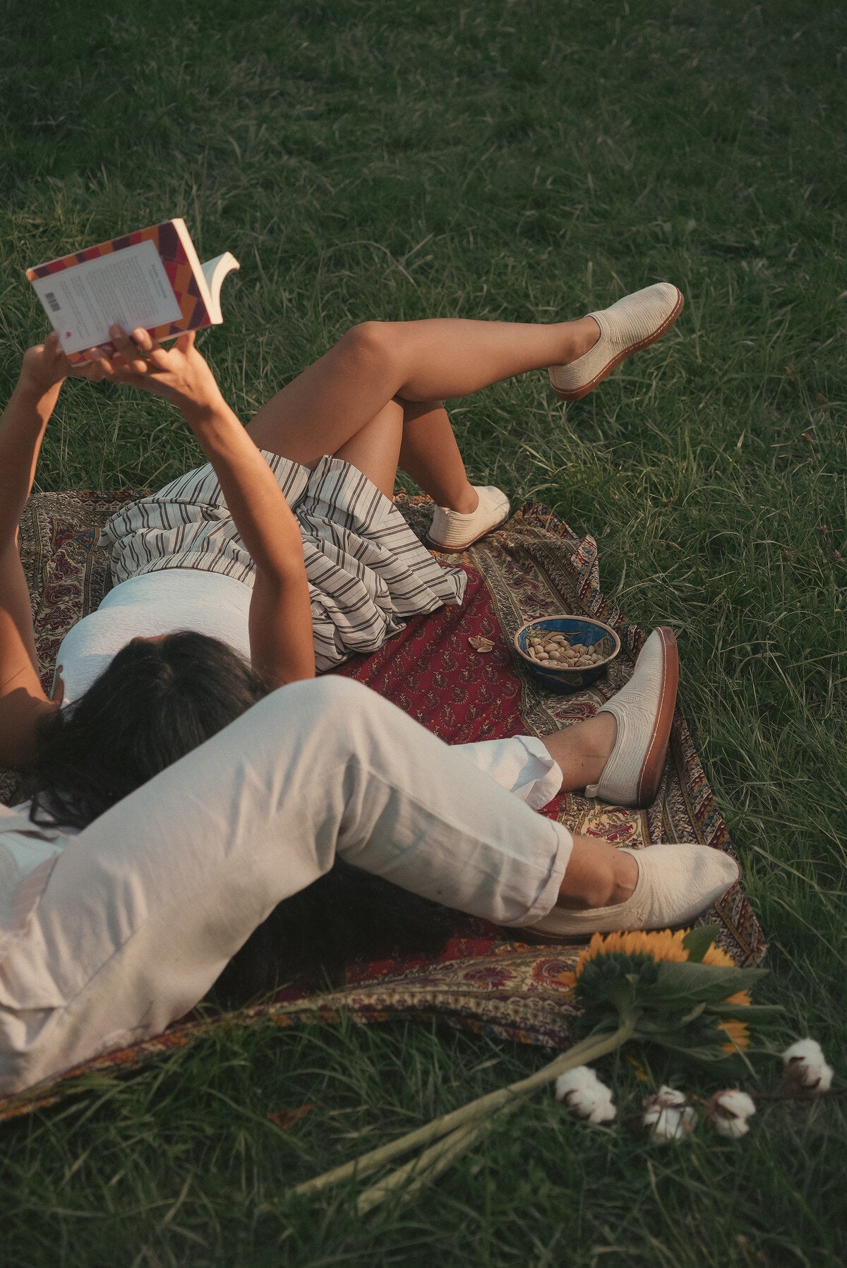 Lecture allongée sur un tapis dans l'herbe, pâpouches aux pieds