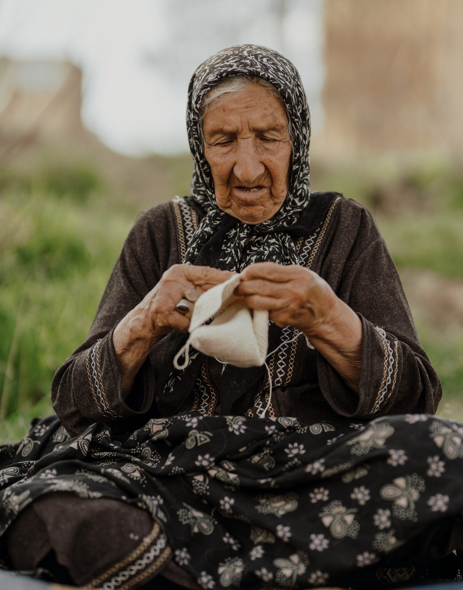 Artisane aînée crochetant une pâpouche, assise dans l'herbe